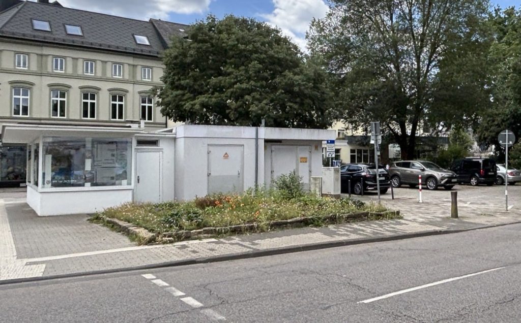 ein weißen kioskähnliches Gebäude auf einem Parkplatz. 
